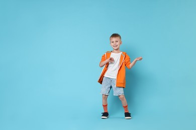 Photo of Happy little boy dancing on light blue background. Space for text