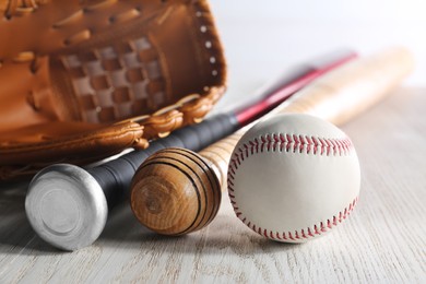 Photo of Baseball glove, bats and ball on white wooden table, closeup