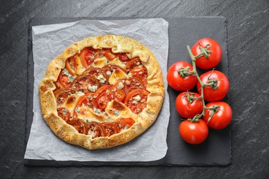 Photo of Tasty galette with tomato and cheese (Caprese galette) on dark textured table, top view