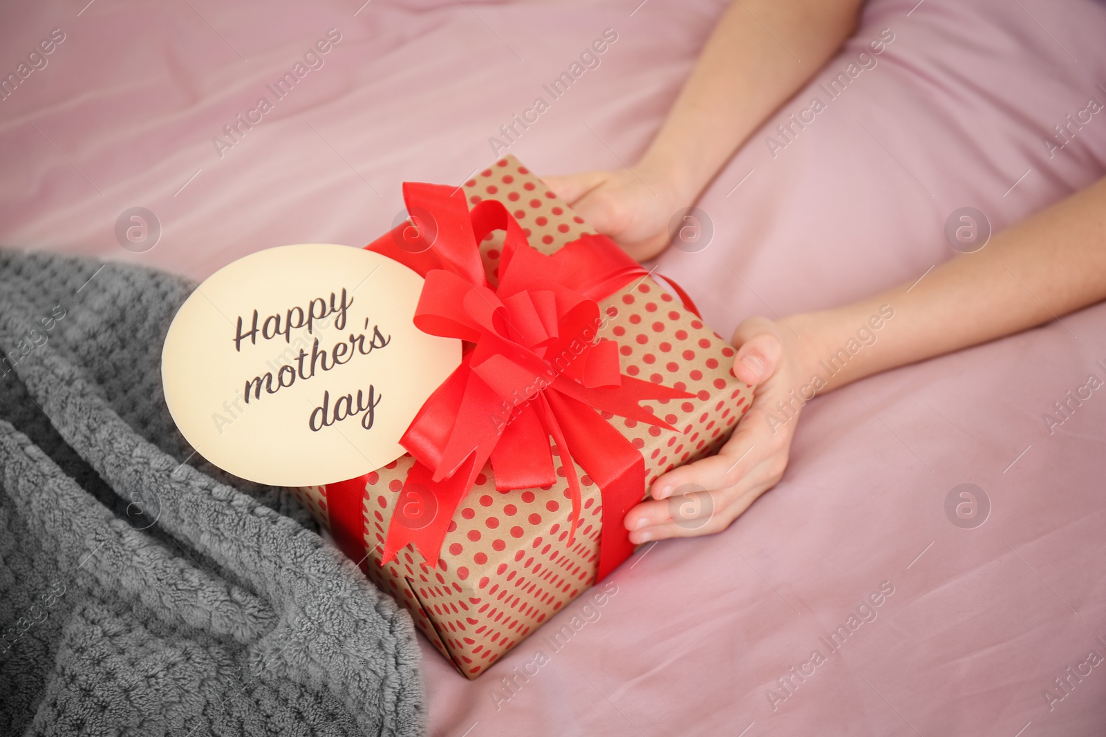 Photo of Little child putting gift box for Mother's Day on bed