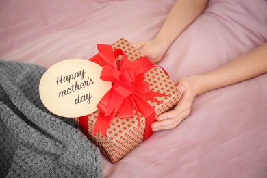 Photo of Little child putting gift box for Mother's Day on bed