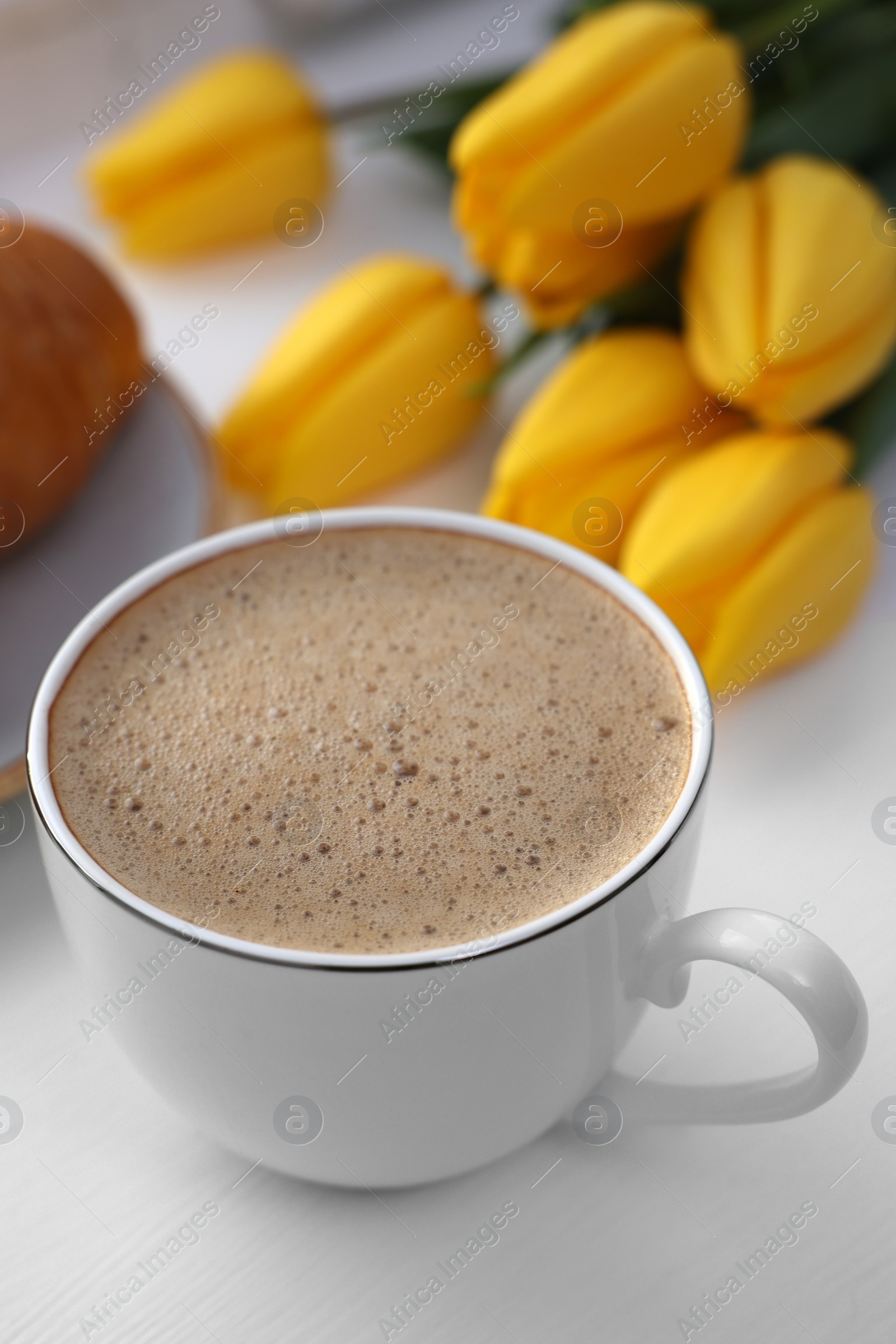 Photo of Delicious morning coffee and flowers on white table, closeup