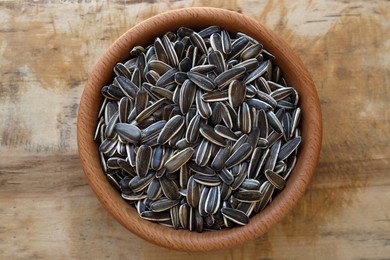 Photo of Bowl with organic sunflower seeds on wooden table, top view