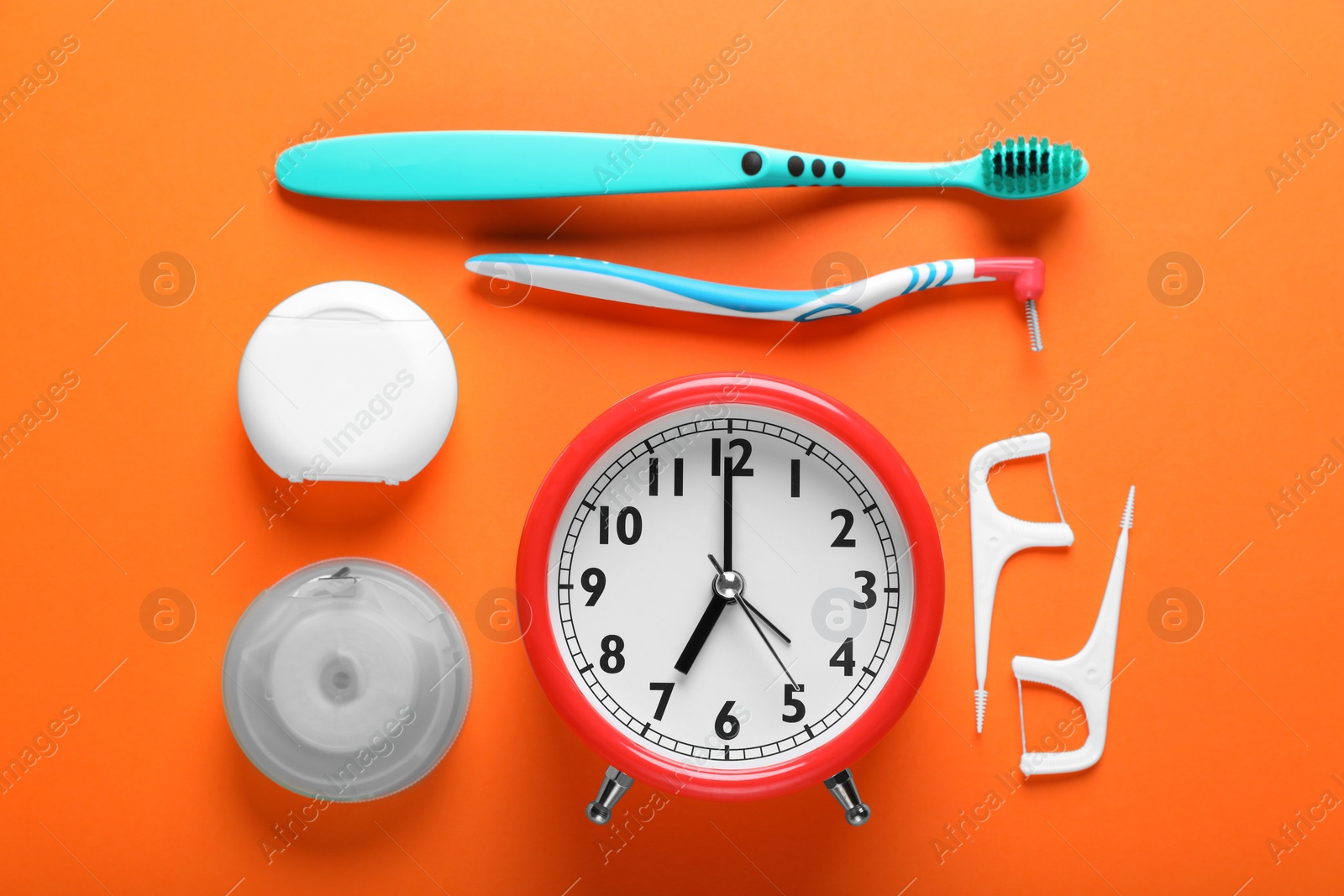 Photo of Flat lay composition with dental flosses, alarm clock and different teeth care products on orange background