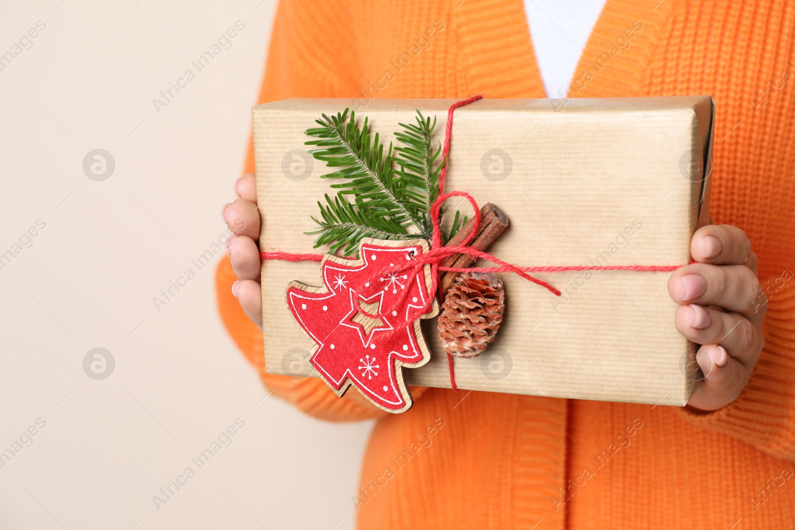 Photo of Woman holding beautifully wrapped Christmas gift box on beige background, closeup. Space for text