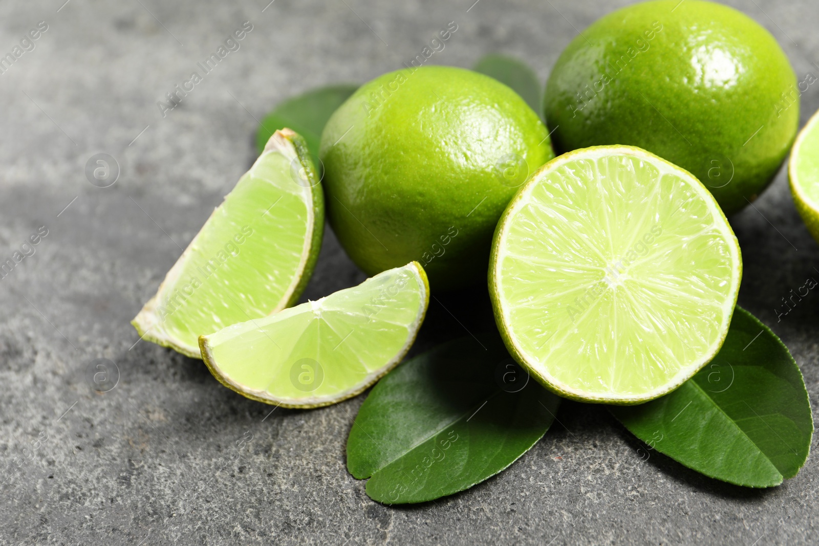 Photo of Fresh ripe limes and leaves on grey table, closeup