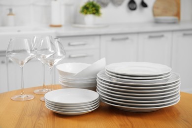 Photo of Clean plates, bowls and glasses on wooden table in kitchen