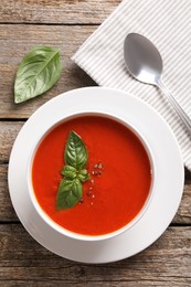 Delicious tomato soup with basil, spices and spoon on wooden table, flat lay