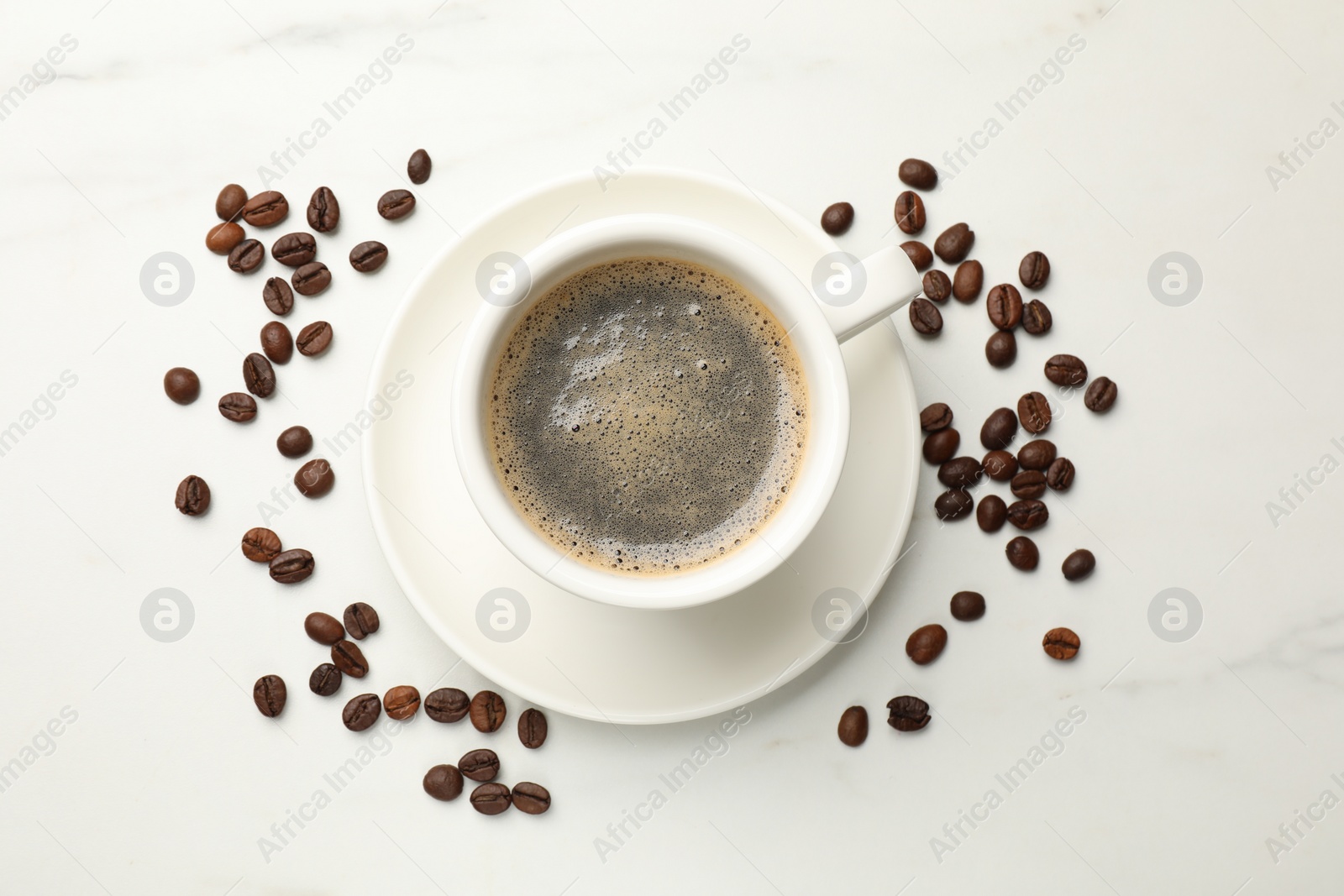 Photo of Cup of aromatic coffee and beans on white table, top view
