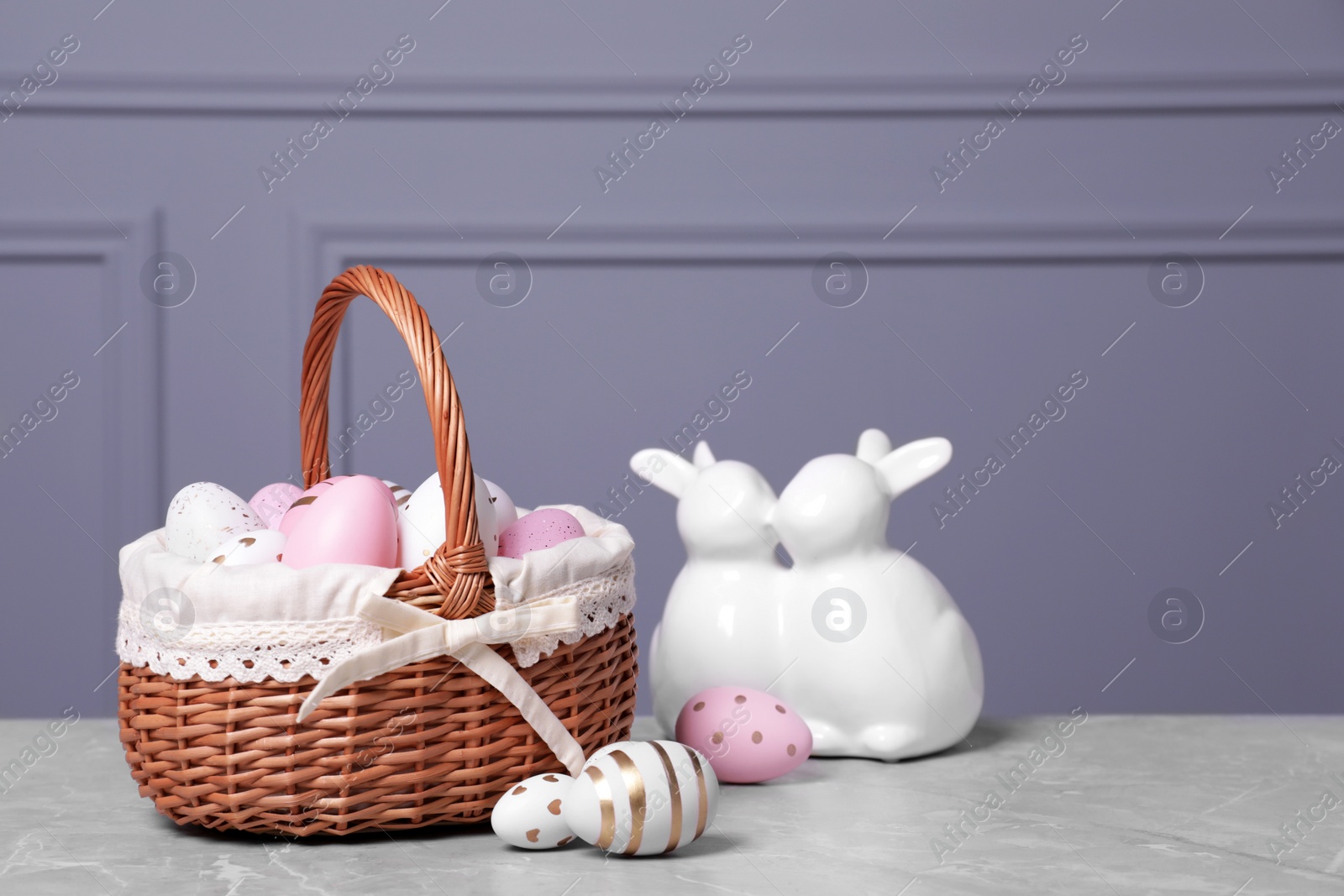 Photo of Easter basket with many painted eggs and figure of rabbits on grey textured table. Space for text