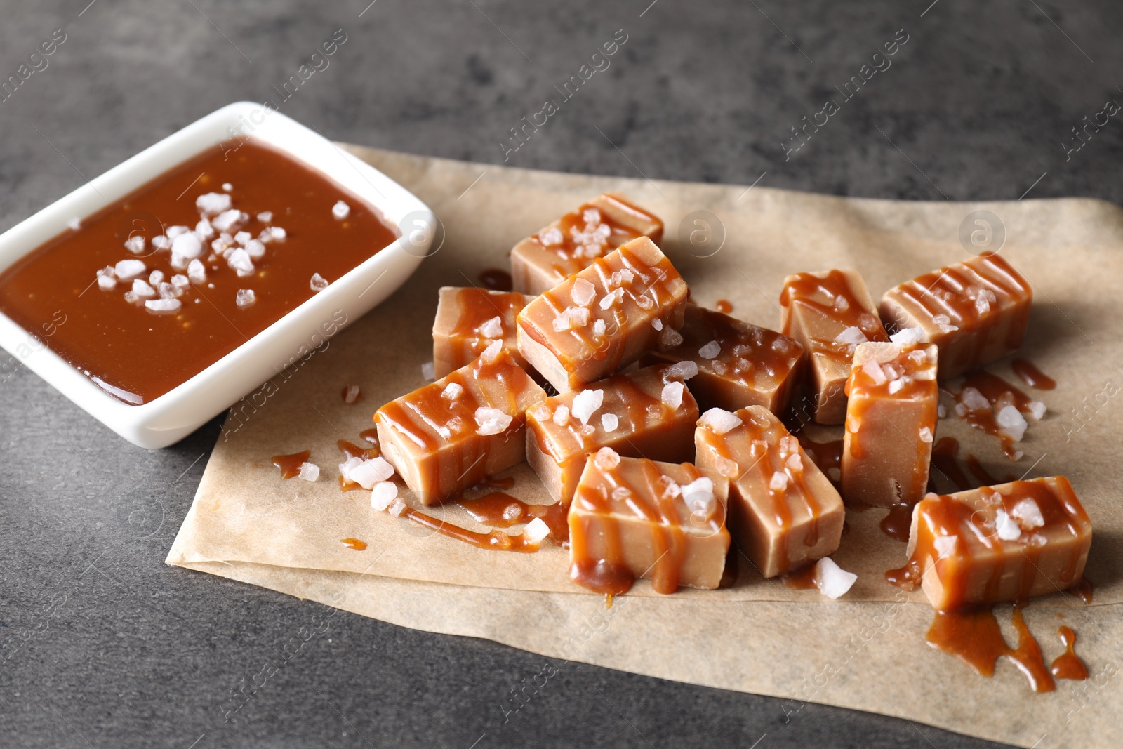 Photo of Tasty candies, caramel sauce and salt on grey table