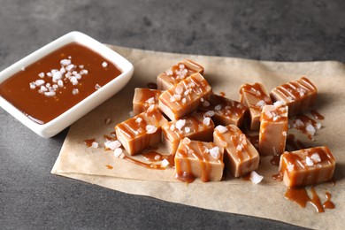 Tasty candies, caramel sauce and salt on grey table