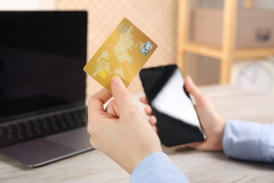Photo of Online payment. Woman using credit card and smartphone near laptop at light wooden table indoors, closeup