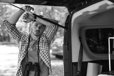 Young man with binoculars near van outdoors, black and white effect. Camping season