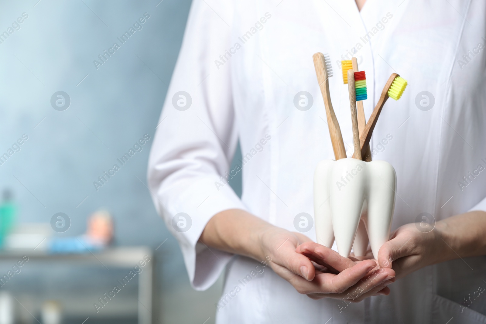 Photo of Dentist with wooden toothbrushes in ceramic holder on blurred background, closeup view. Space for text