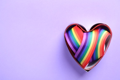 Heart shaped mold and bright rainbow ribbon on color background, top view with space for text. Symbol of gay community