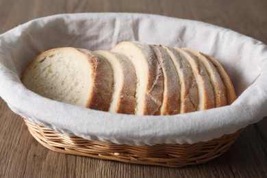 Photo of Fresh bread slices in wicker basket on wooden table, closeup