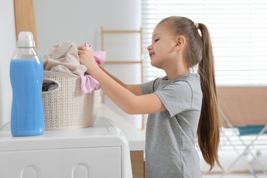 Little girl taking out dirty clothes from basket in bathroom