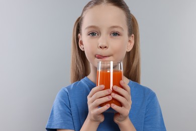 Photo of Cute little girl enjoying fresh juice on light gray background