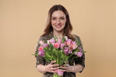 Happy young woman holding bouquet of beautiful tulips on beige background