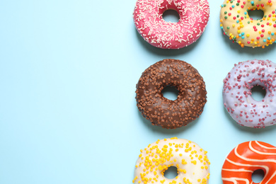 Photo of Delicious glazed donuts on light blue background, flat lay. Space for text