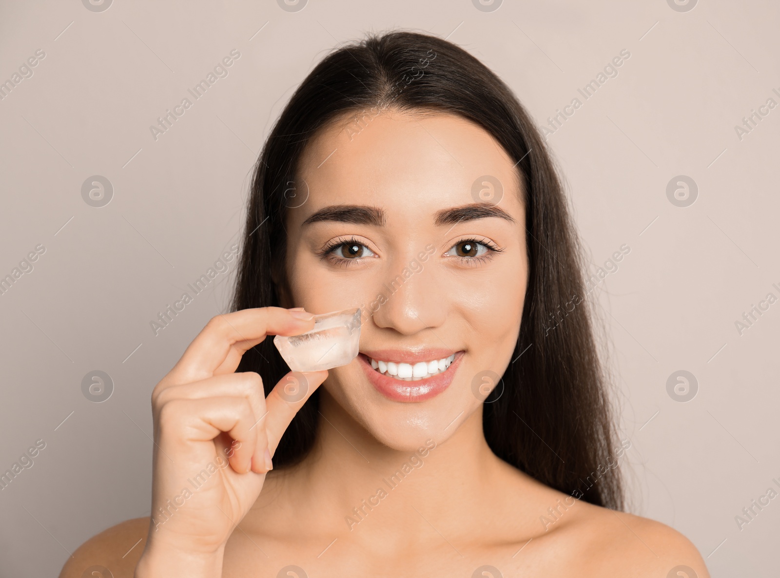 Photo of Young woman with ice cube on light background. Skin care