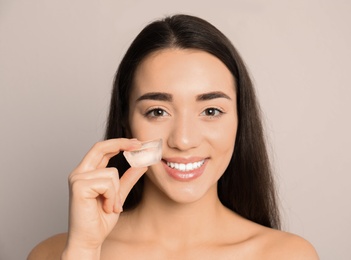 Young woman with ice cube on light background. Skin care