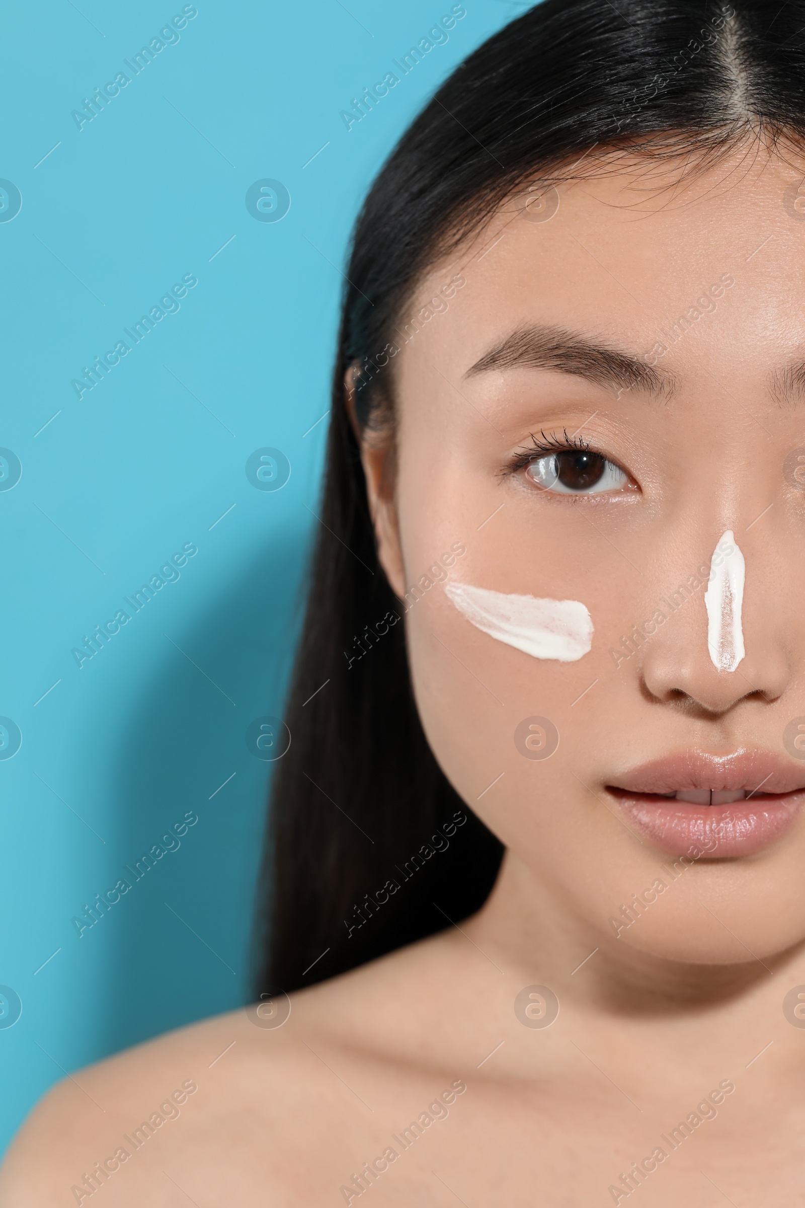 Photo of Beautiful young woman with sun protection cream on her face against light blue background, closeup. Space for text