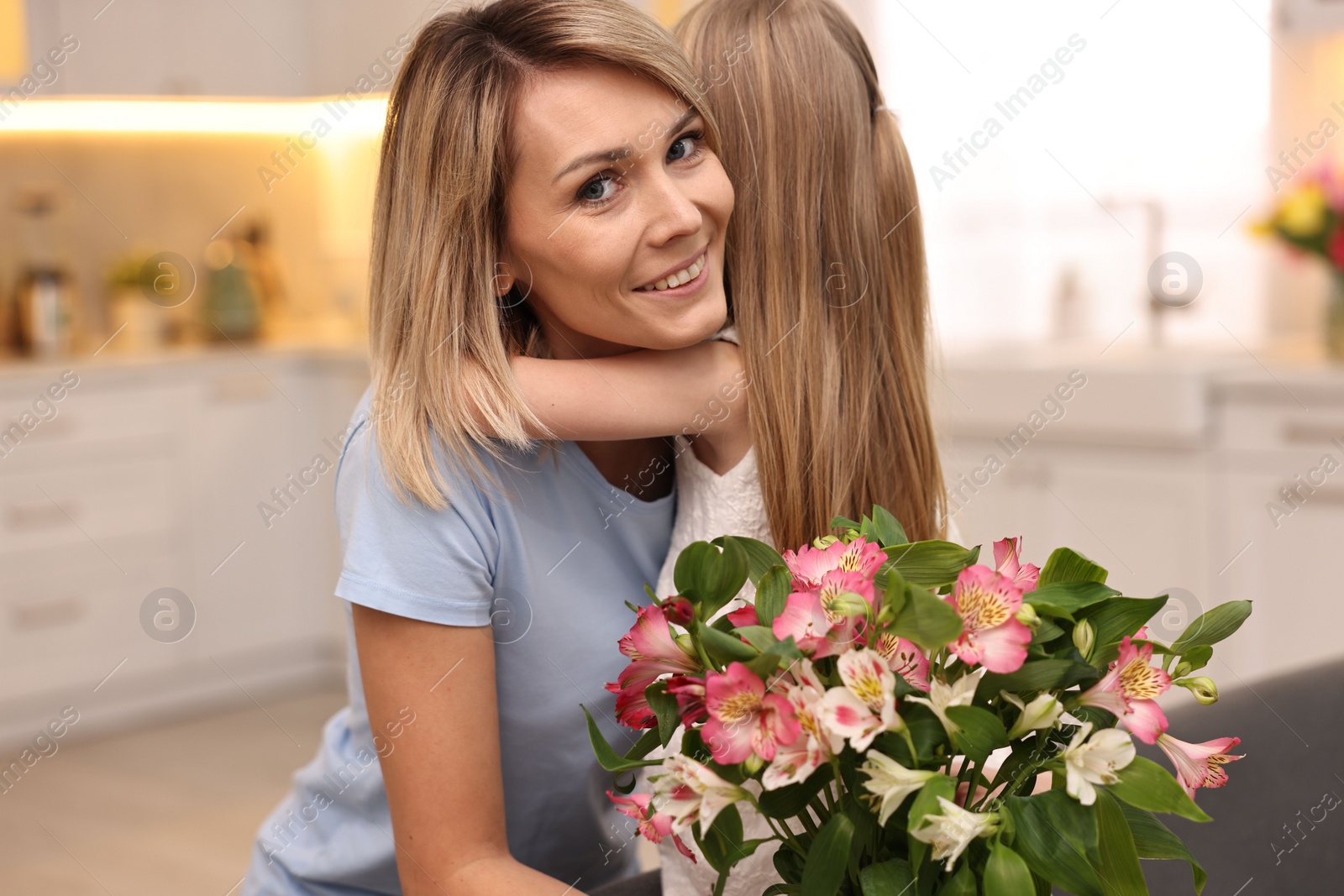 Photo of Little daughter congratulating her mom with bouquet of alstroemeria flowers in kitchen. Happy Mother's Day