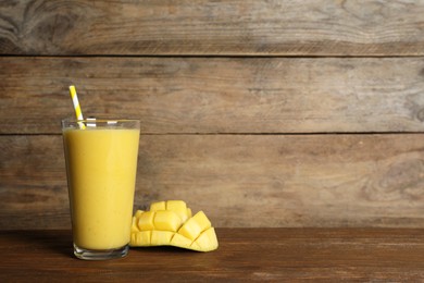 Glass of tasty smoothie with straw and mango on wooden table. Space for text