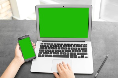 Woman using laptop and smartphone at desk, closeup. Devices displays with chroma key