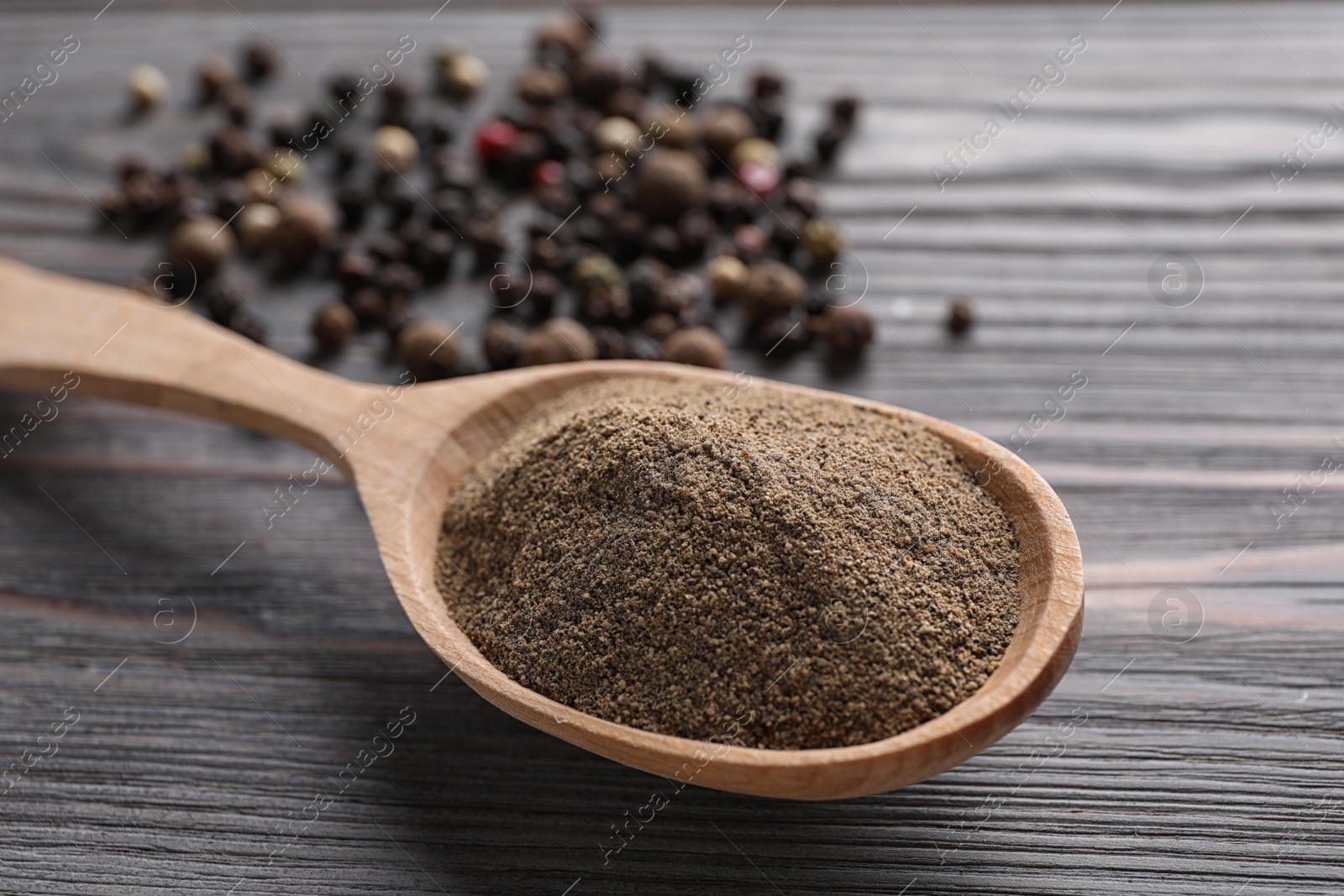 Photo of Ground pepper in spoon on wooden table, closeup