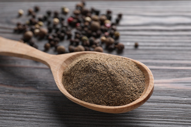 Photo of Ground pepper in spoon on wooden table, closeup