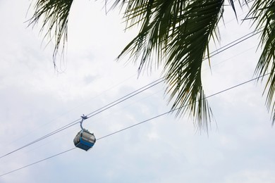 Cableway with cabin against cloudy sky, low angle view