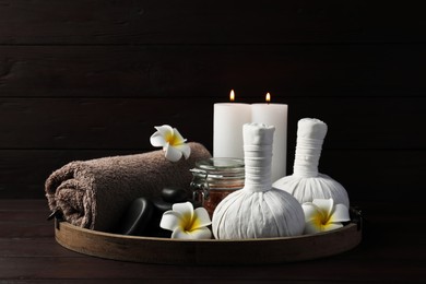Photo of Herbal massage bags, spa stones, candles, rolled towel, sea salt and plumeria flowers on wooden table