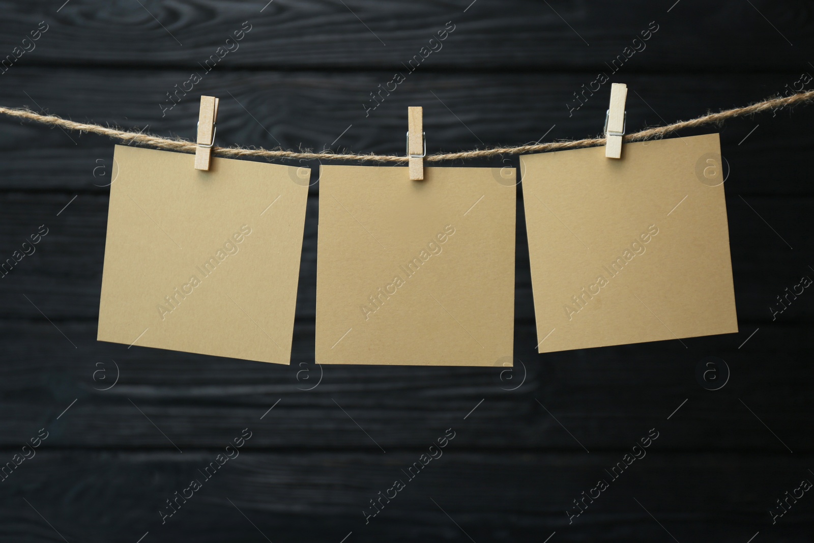 Photo of Clothespin with blank notepapers on twine against black wooden background. Space for text