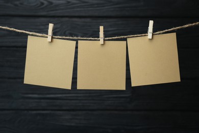 Photo of Clothespin with blank notepapers on twine against black wooden background. Space for text