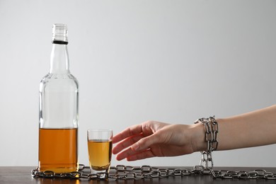 Photo of Addicted woman chained to bottle of alcoholic drink at wooden table against white background, closeup