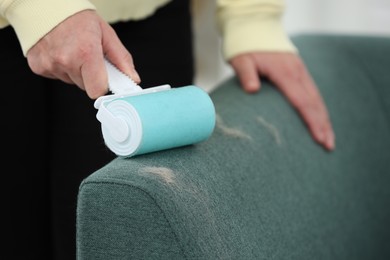 Photo of Woman with lint roller removing pet hair from sofa indoors, closeup