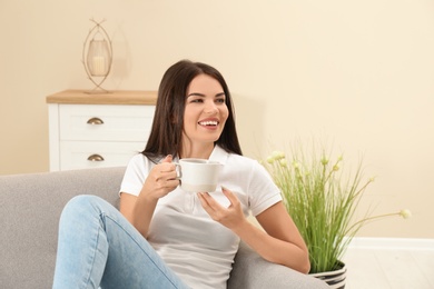 Photo of Beautiful woman with cup sitting on sofa at home