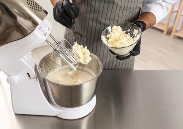 Photo of Male pastry chef preparing dough in mixer at kitchen table, closeup