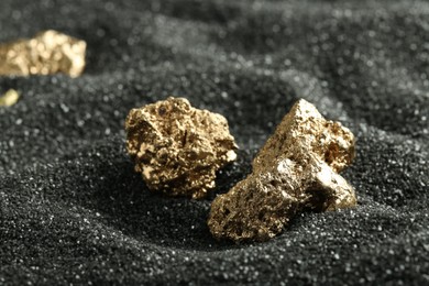 Photo of Shiny gold nuggets on black sand, closeup