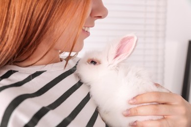 Photo of Woman with fluffy white rabbit indoors, closeup. Cute pet