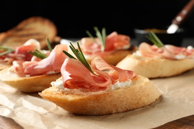 Photo of Tasty bruschettas with prosciutto and cream cheese served on table against dark background, closeup. Space for text