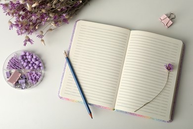 Photo of Open notebook, flowers and stationery on white table, flat lay. Personal planning