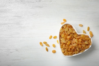 Photo of Bowl of raisins on wooden background, top view with space for text. Dried fruit as healthy snack