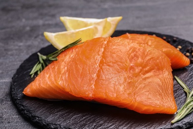 Photo of Slate plate with salmon fillet on grey table, closeup