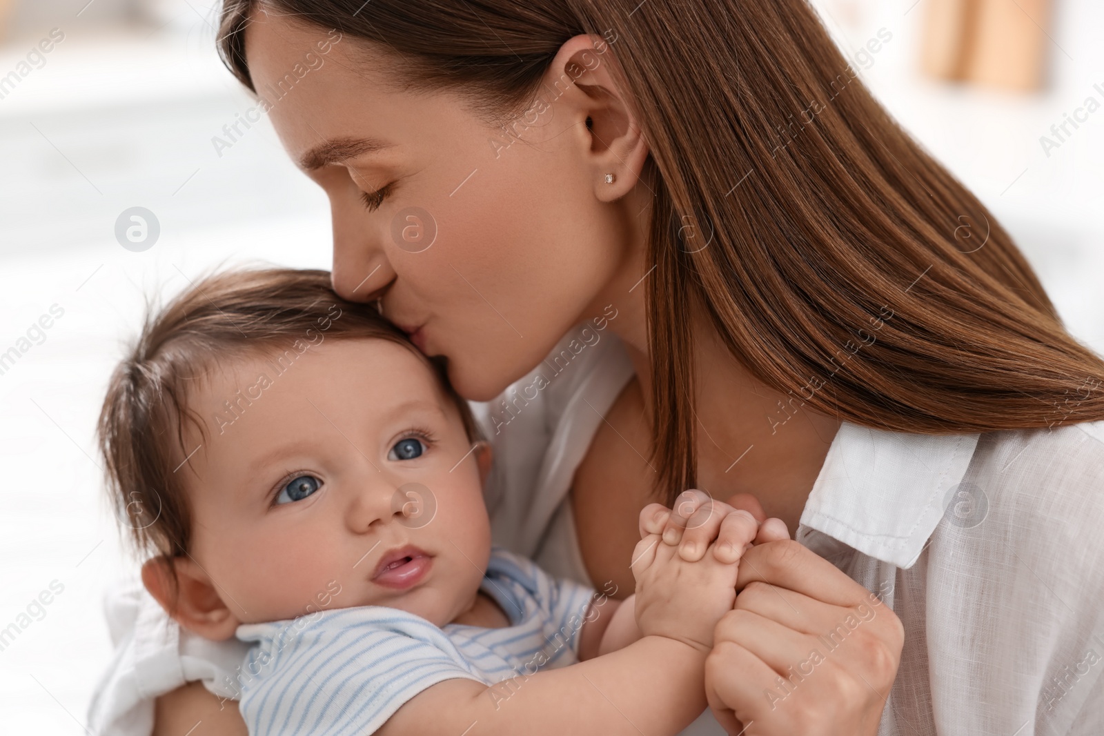 Photo of Happy mother kissing her little baby indoors, closeup