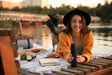 Young woman with thermos spending time on pier at picnic