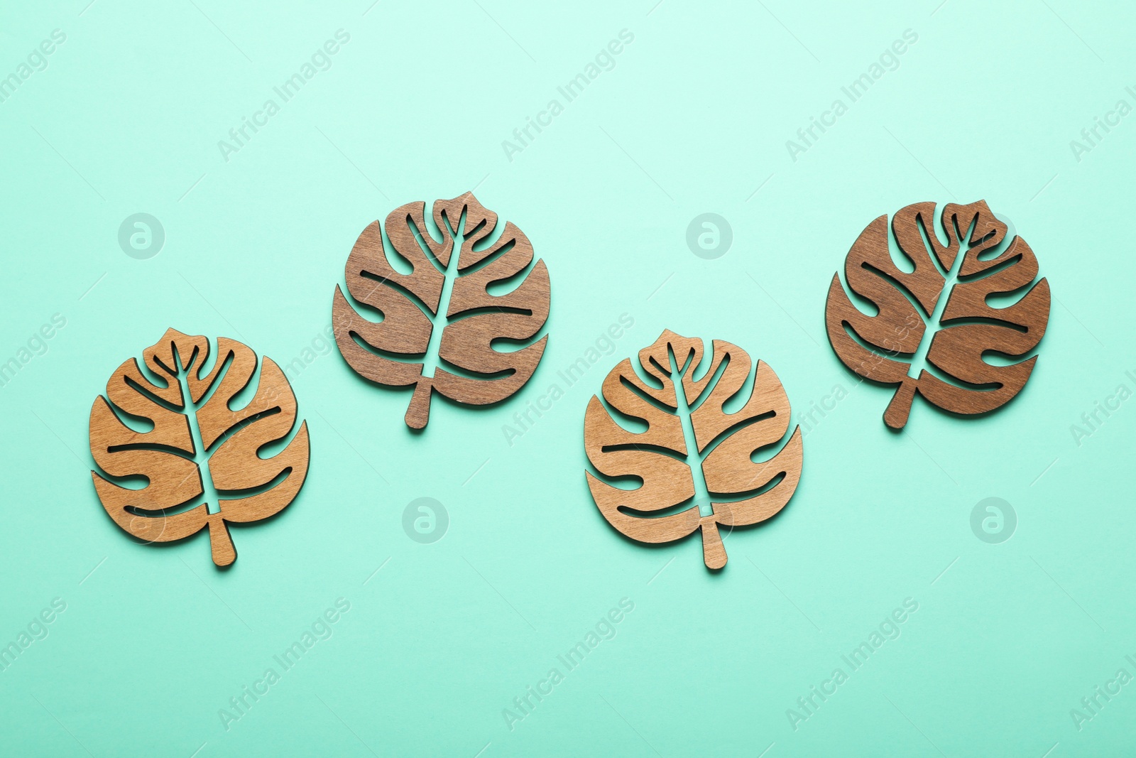 Photo of Leaf shaped wooden cup coasters on turquoise background, flat lay